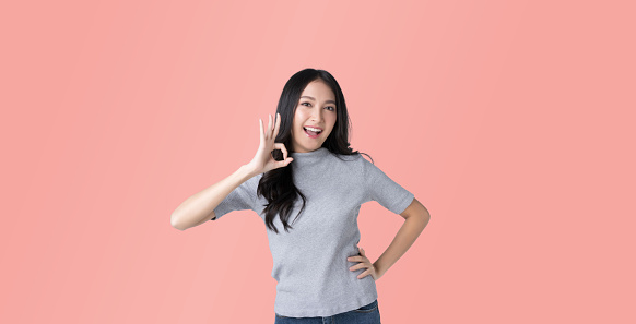 Young Asian woman showing ok sign on hand isolated pink color background