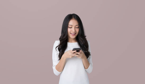 istock Young Asian woman texting message using mobile phone application on isolated brown background 1480985986