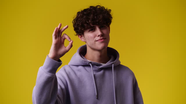 4k video of man showing OK sign on yellow background.