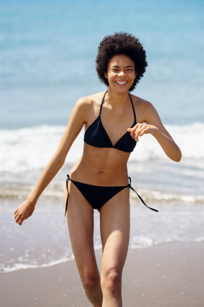 istock Joyful black woman in bikini walking along seaside 1480996432