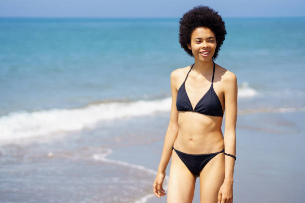 istock Content black woman in bikini walking on seashore 1480996434