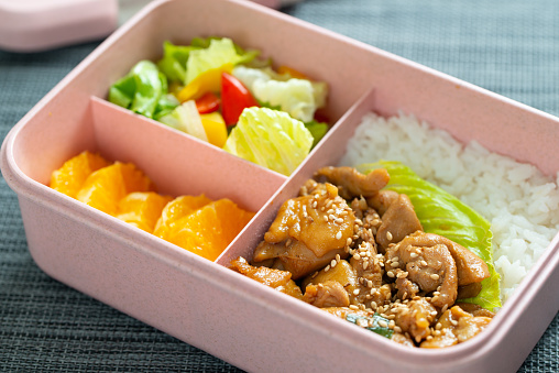 Kid school lunch bento box set of sesame chicken, rice, salad and orange slices