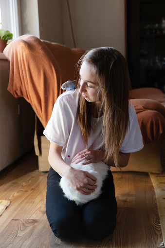 Young girl holding her white fluffy pet rabbit and a parakeet on her shoulder.