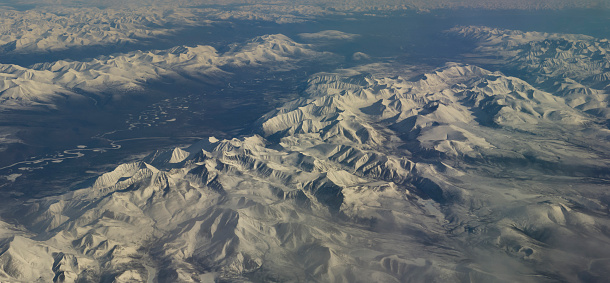 Russia. Eastern Siberia. View from the window of the plane to the snow-capped peaks of the mountains on the high plateau of the Irkutsk region.