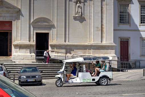 Coimbra, Portugal - August 15, 2022: Tuk-tuk electric tour vehicle with driver and family of tourists outside University of Comibra