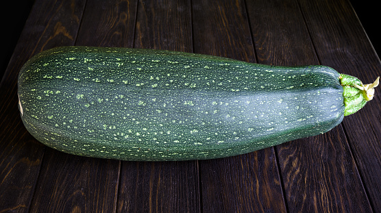 Vegetable marrow zucchini on vintage wooden table. Photography of one big fresh squash isolated on dark planks. Theme of zucchini, organic food, nature, summer, farm.