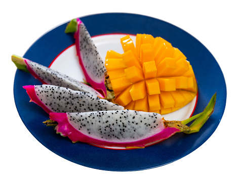 Healthy colorful vibrant snack of tropical fruits. Slices of yellow-orange mango and pink pitaya with small black seeds on plate. Isolated over white background