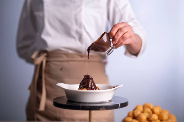 Female chef pouring chocolate sauce on profiteroles stock photo