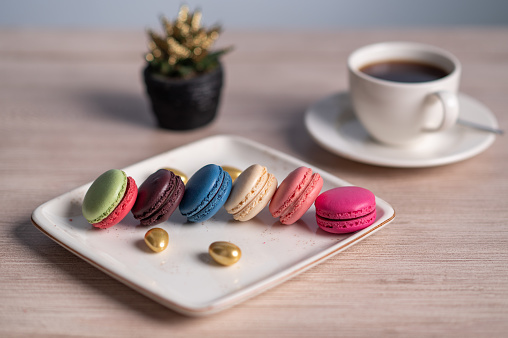Colorful macarons on a plate with a cup of coffee.