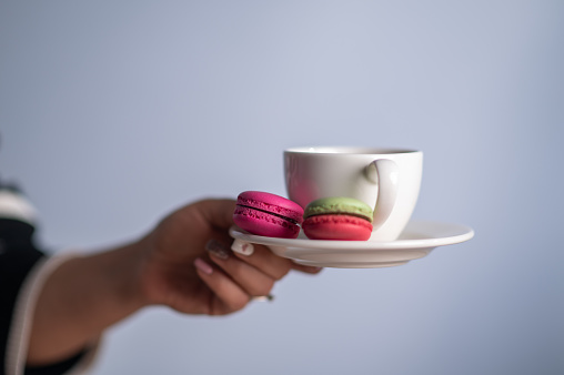 A woman hand holding coffee cup with macarons.