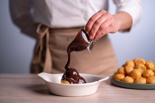 Female chef pouring chocolate sauce on profiteroles.