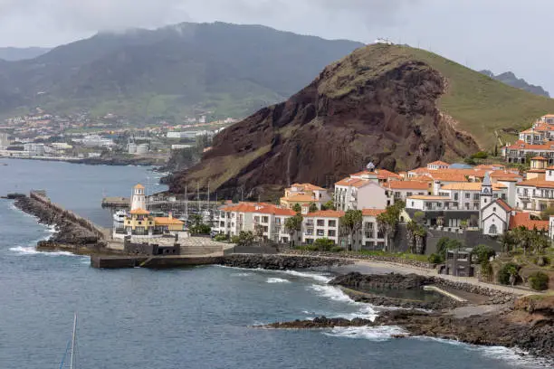 A rural village perched atop a hill, with picturesque architecture and lush trees surrounded by winding roads. Madeira, Portugal