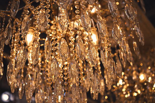 Crystal chandelier close-up. Glamour background with copy space. Warm light and low key image. Selective focus and bokeh.