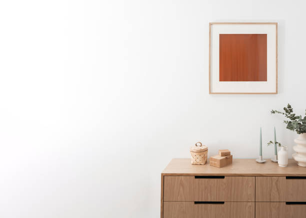 eucalyptus branches in ceramic vase, candlestick and bamboo jewelry box on wooden chest of drawers and picture in frame on wall in living room with elegant interior