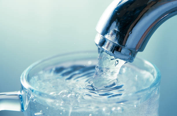 vue rapprochée de l’eau qui coule du robinet dans le verre - eau potable photos et images de collection