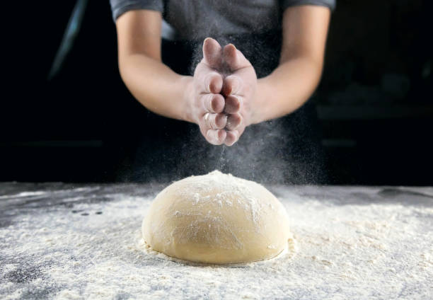 istock Making bread, kneading the dough. Hands on a dark background sprinkle flour on brightly lit dough. 1481042378