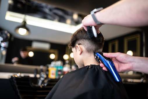 Little 7-year-old boy goes to a barbershop to get a modern haircut, indoors store working hairdresser real image