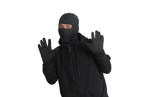 Mysterious thief man wearing black hoodie and mask was caught while sneaking around. Shocked and frightened criminal. Isolated image on gray background