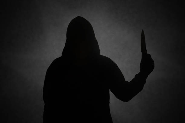 Mysterious man wearing black hoodie holding a knife to stab someone. Crimes and criminality concept stock photo