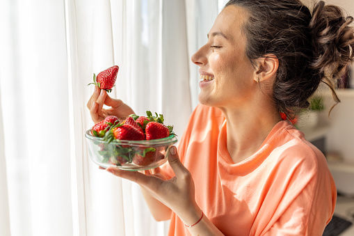 For a healthy and satisfying snack, this young woman turns to fresh strawberries! She's enjoying them in her bright and cheerful kitchen