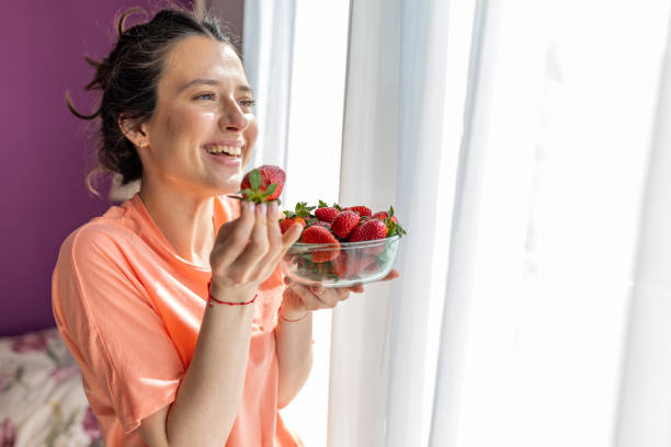istock Young Woman Nibbling on Fresh Strawberries in Kitchen 1481055099