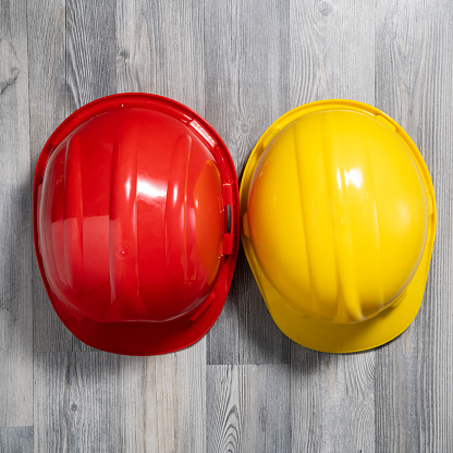 High angle close up photo of red and yellow work helmets on gray wooden background. No people are seen in frame. Shot under daylight.