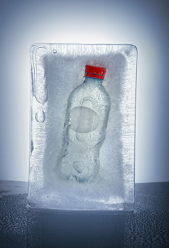 Bottle frozen in a piece of ice. Bubbles and cracks in the ice, vertical photo.