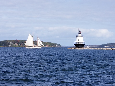 The lighthouse at Spring Point Ledge in Maine with a sailboat.