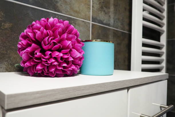 Interior of a modern bathroom with a white tile wall, washstand, towel and toothbrushes. Glass vase with pink flowers that stand out on white background. The concept of bathroom, copy space