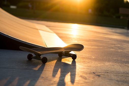 A lone skateboard is sitting upright beside a skateboard ramp at a park at sunset.