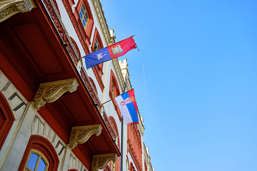 Flags on a facade of Rectorate building of Belgrade University. Serbian national flag on historical building facade. Low angle view.