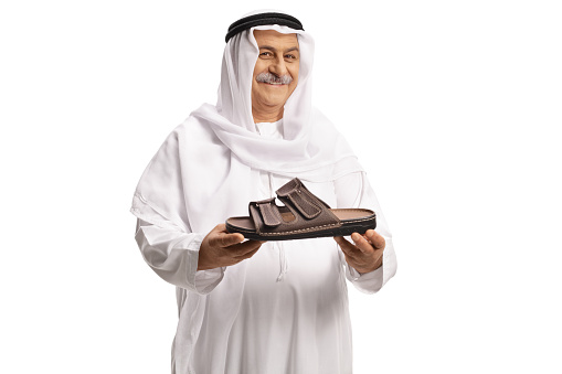 Arab man holding a brown leather sandal and smiling isolated on white background