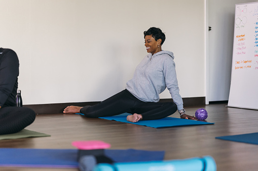 A beautiful African American woman sits on a yoga mat doing warm-up stretches before a group yoga class
