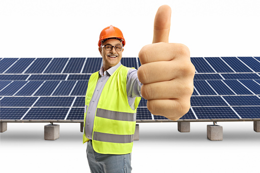 Cheerful mature male engineer showing thumbs up at a solar farm isolated on white background