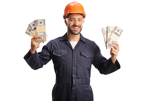 Factory worker wearing a protective helmet and goggles and holding stacks of money isolated on white background