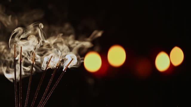 A closeup of burning incense sticks with smoke over a black blur background