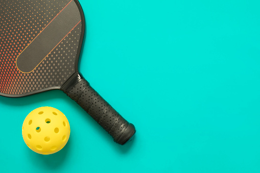 Closeup top view on pickleball paddle and a ball on light aqua blue background with copy space