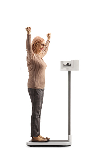 Full length side shot of a happy woman weighing on a medical scale and gesturing happiness isolated on white background