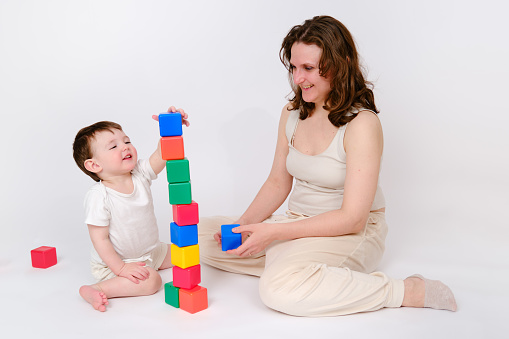 mother and daughter play with wooden cubes, with letters on the faces and able to hold smaller ones; the room is bright and clear