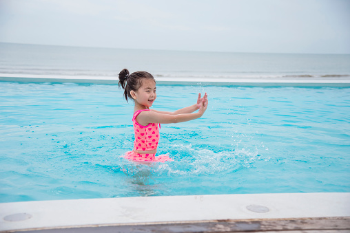 Toddler girl Kid swim playful in swimming pool summer time with pink swimwear in blue water at hotel swimming pool outdoor. Happy girl swim playful water splash with happiness on summer vacation