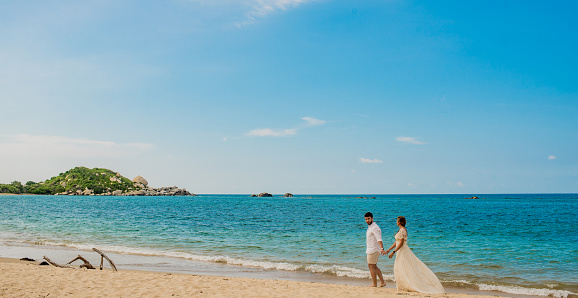 a couple dressed in white walking along the shore of the palaya holding hands
