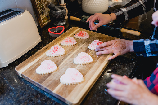 Mother and daughter bonding at home together as they work together in the kitchen making home made heart shaped cookies. Concepts shown are team work, togetherness, connection and balanced lifestyle.