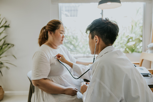 Asian transgender man doctor listening patient heartbeat before staring consult on nutrition for overweight person.