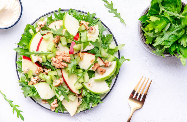 istock Waldorf salad with red and green apple, green celery, lettuce, arugula and walnuts on plate, white table background, top view 1481101062