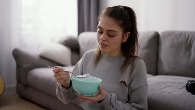 Woman eating a bowl of oatmeal sitting on floor