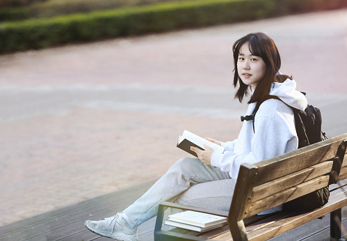 High school student and college student concept with backpack sitting on a park bench and reading and studying