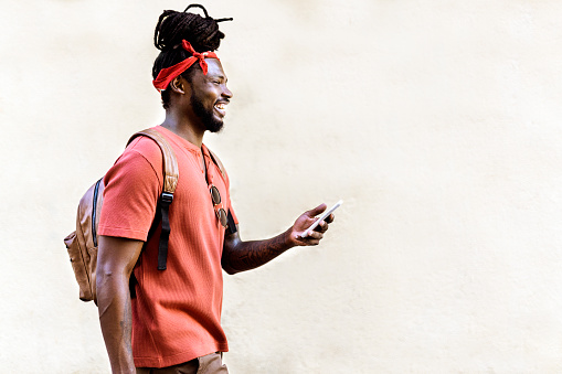Stock photo of smiley african american boy with dreadlocks and a bandana walking in the street and using his phone.