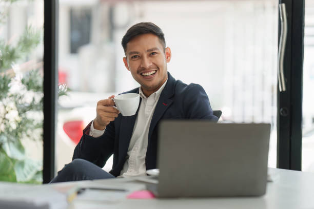 istock Smiling Asian Banker makes financial report and studies annual figures, analyzes profits. Accountant checks status of financial 1481112844