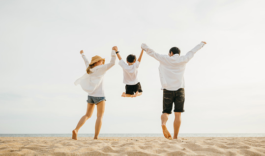 Back family mother, father and son holding hands and jumping in air at dawn time, Family outdoor activities, Happy Asian family people have fun healthy lifestyle together on beach, holiday vacation