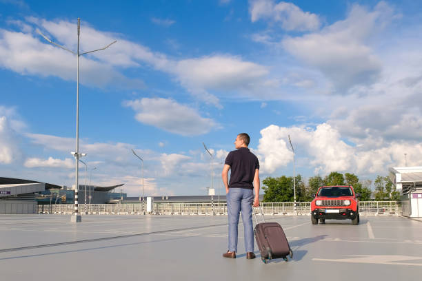 jeune homme avec une valise dans un parking par une journée ensoleillée - parking sign taxi taxi sign cloud photos et images de collection